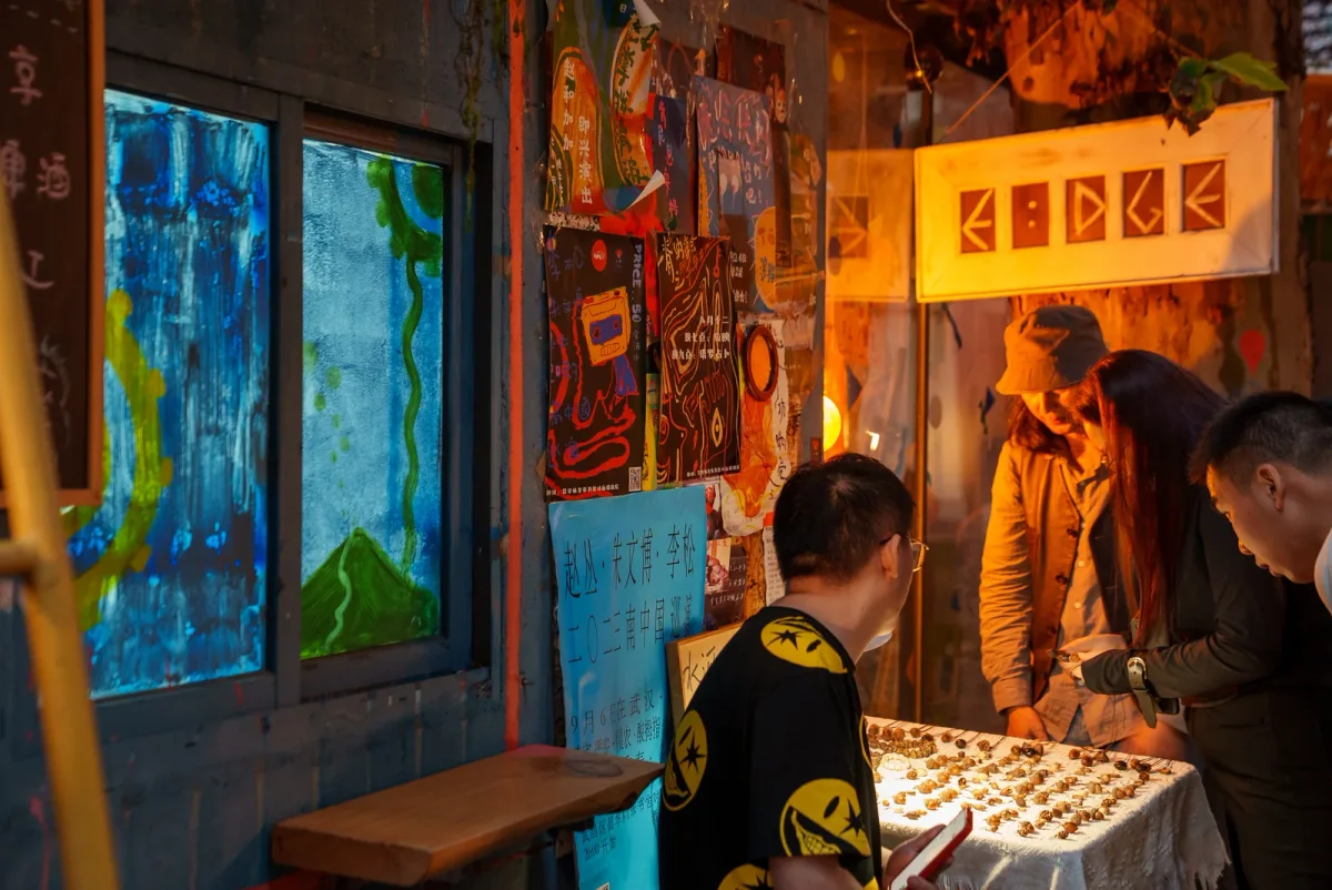 武汉街边一家名为EDGE的店铺前，三名顾客围在摆满小物件的摊架旁挑选物品，背景墙壁贴满海报与涂鸦。